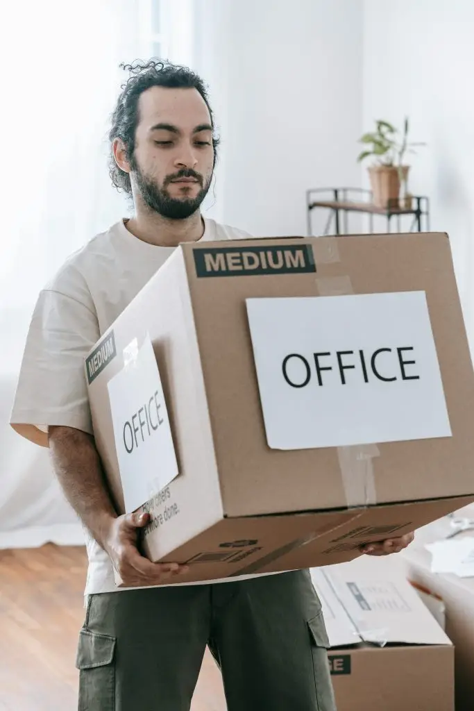 Man moving box labeled 'Office' indoors during relocation or packing.